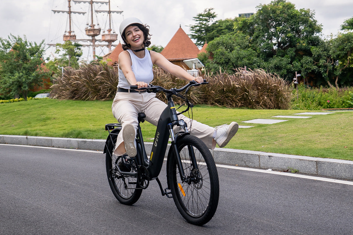 Vrouw op grijze DYU C1 26 Inch stads E-bike met helm, lachend tijdens rit.