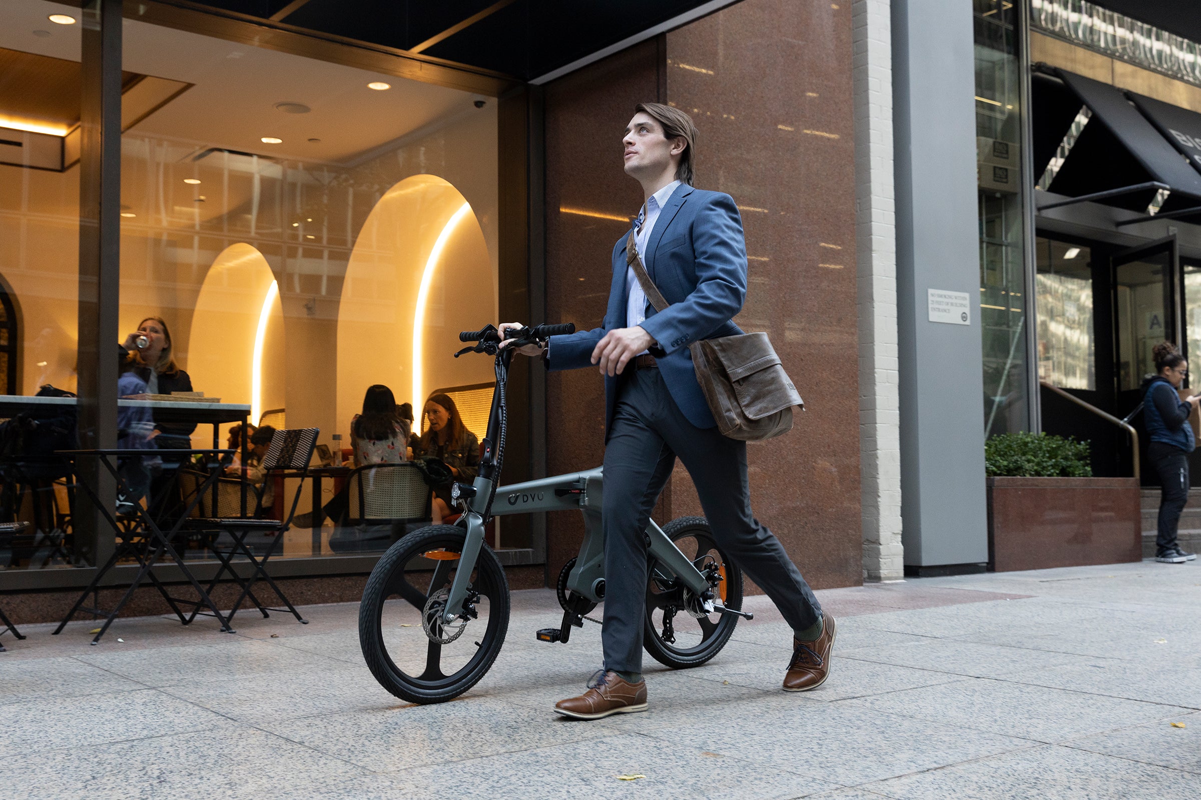 Man in suit walking electric bike T1 outside a stylish cafe.